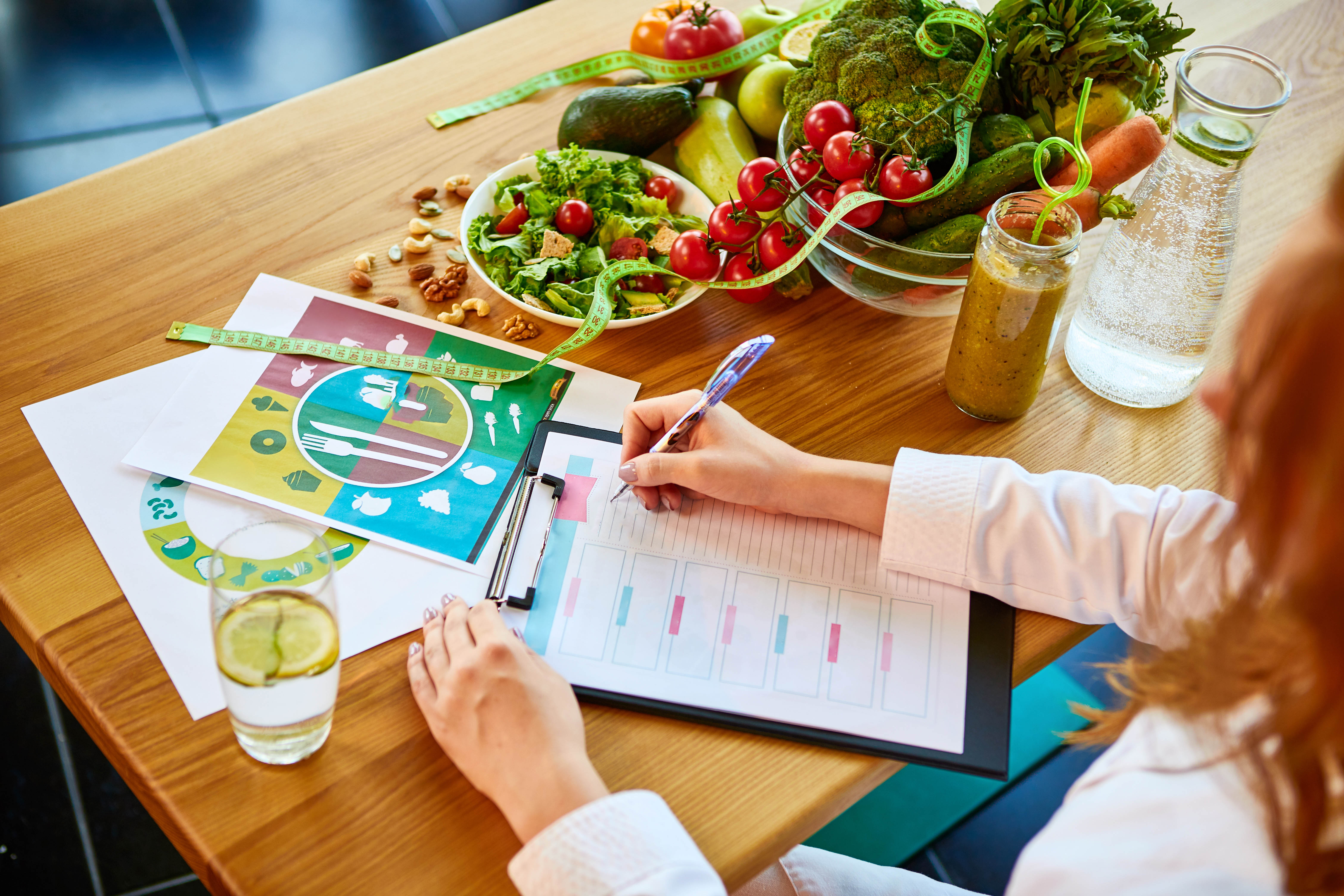 Close-up of the hands of a doctor, creating a nutrition plan with healthy foods on the table Close-up of the hands of a doctor, creating a nutrition plan with healthy foods on the table